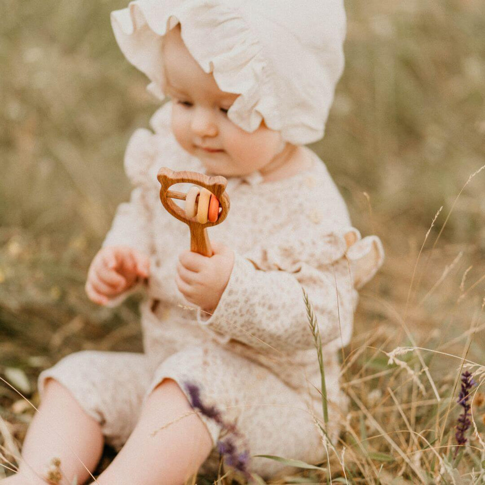 A baby in tall grass holding the wooden bear rattle from Sabo.