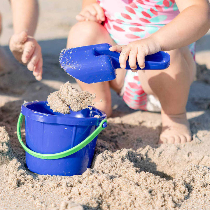Little girl holding a blue Spielstabil Small Sand Scoop putting sand into a blue Spielstabil Pail