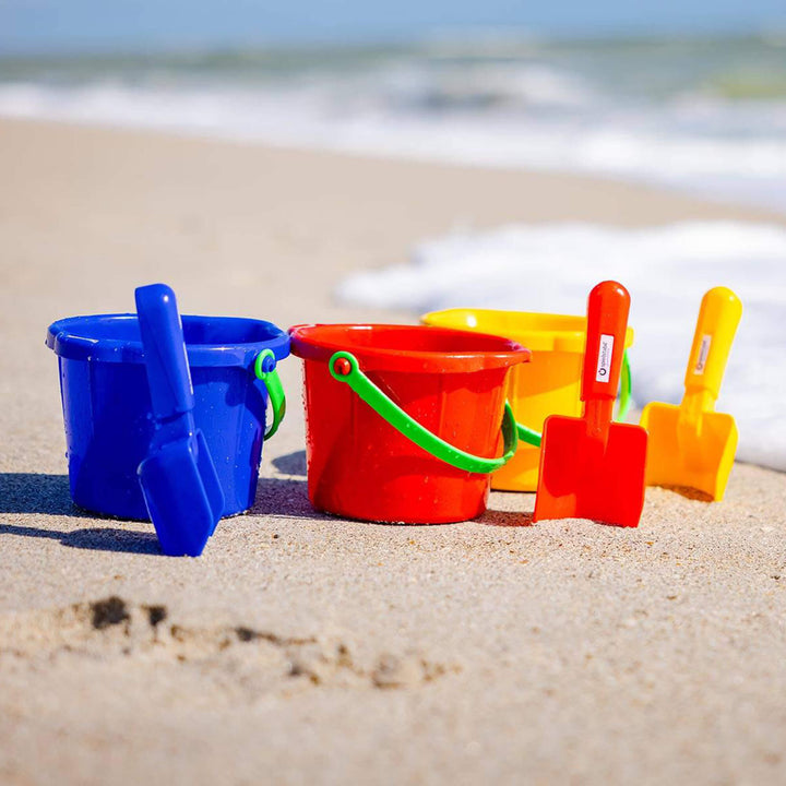 3 small Spielstabil Sand Pails and scoops by the ocean in blue, red, and yellow