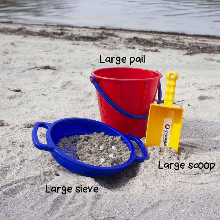 Spielstabil Large Sand Sieve in blue, large pail in red, and large scoop in yellow on the beach