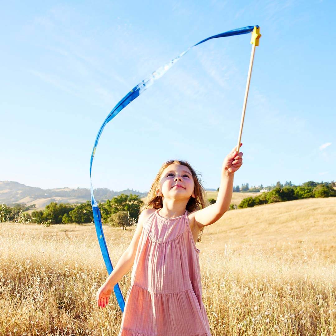 Child playing with a blue star streamer toy in a field on a sunny day.