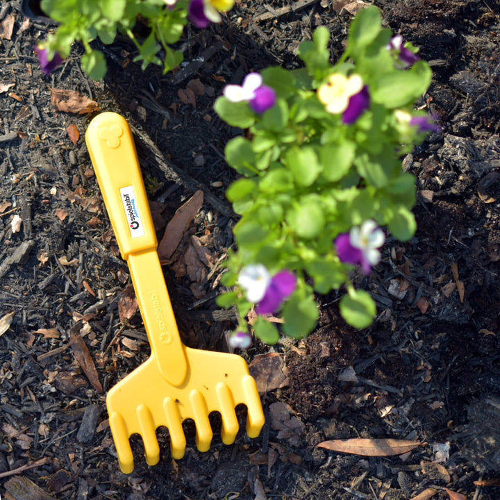 Yellow hand rake laying on mulch with flowers