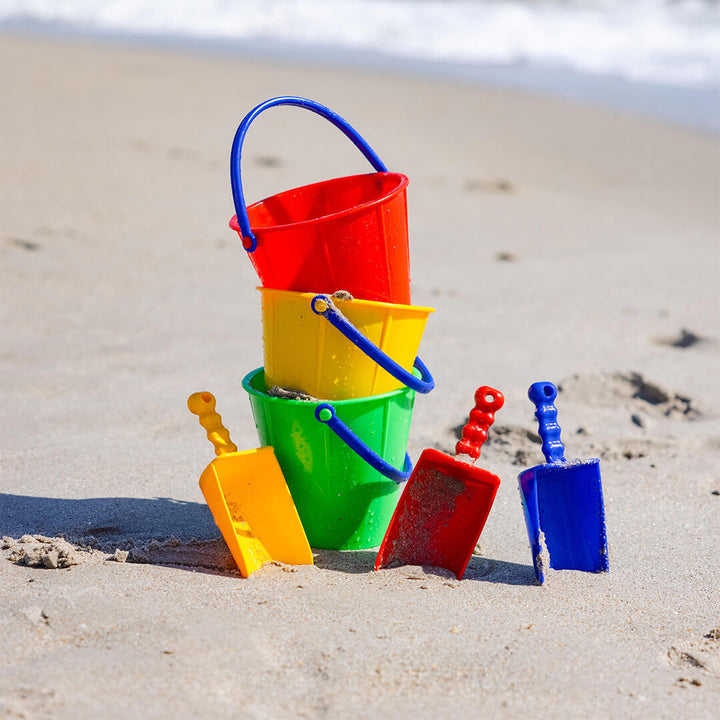 Spielstabil Sand Pails stacked on the beach with sand scoops in yellow, red, and blue