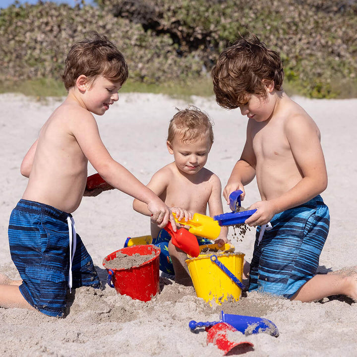 3 boys kneeling in the sand scooping sand into red and yellow Spielstabil Pails with red and yellow Spielstabil Sand Scoops