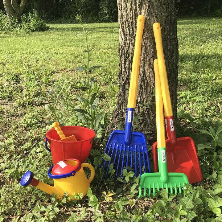 Spielstabil Long Handled Shovel, Garden Rake, and Leaf Rake leaning against a tree with red pail and yellow watering can