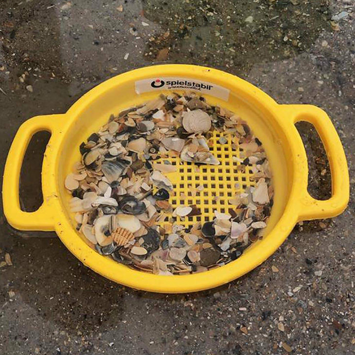 Yellow Spielstabil large sand sieve with shells sitting on the beach