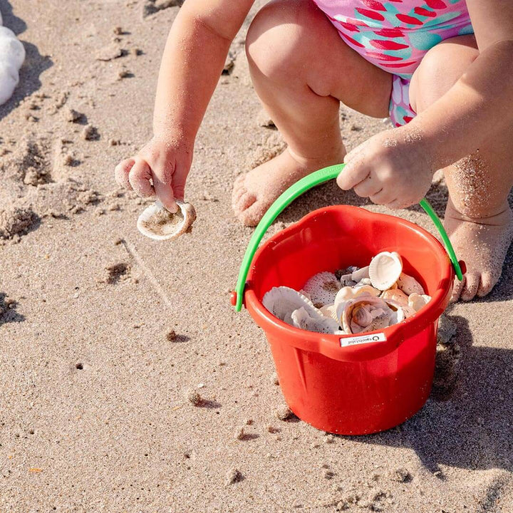 Young girl holding a red Spielstabil Small Sand Pail filled with shells at the beach