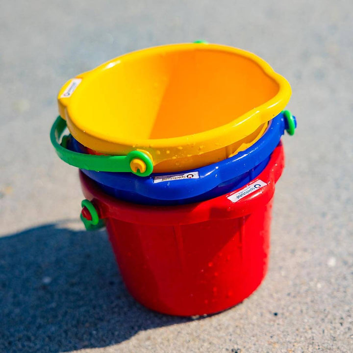 Spielstabil Small Sand Pail in yellow, blue, and red stacked sitting on the sand
