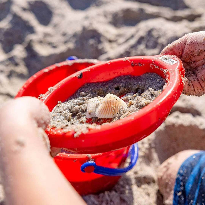 Child sifting sand and beach shells with red sand sieve on the beach