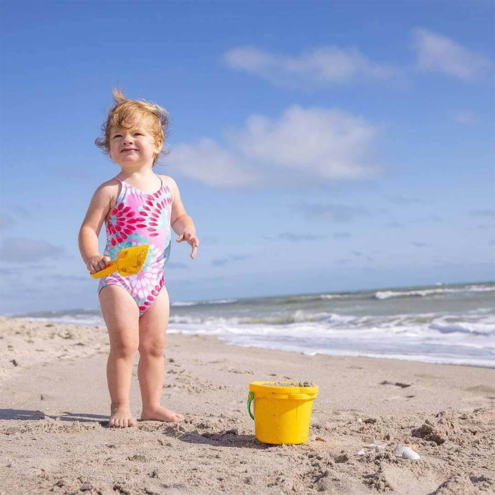 A child standing on the beach with a yellow sand scoop and yellow sand pail