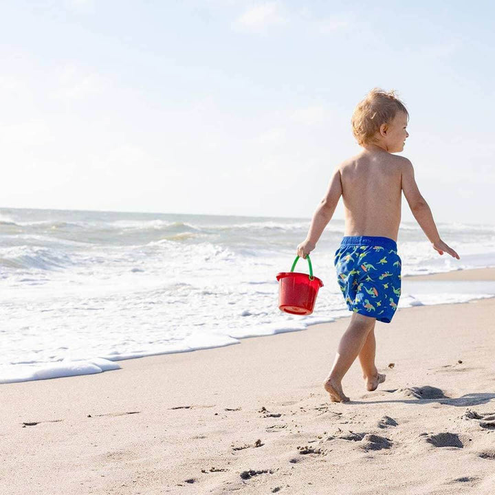 A child walking on the beach holding a red Spielstabil sand pail