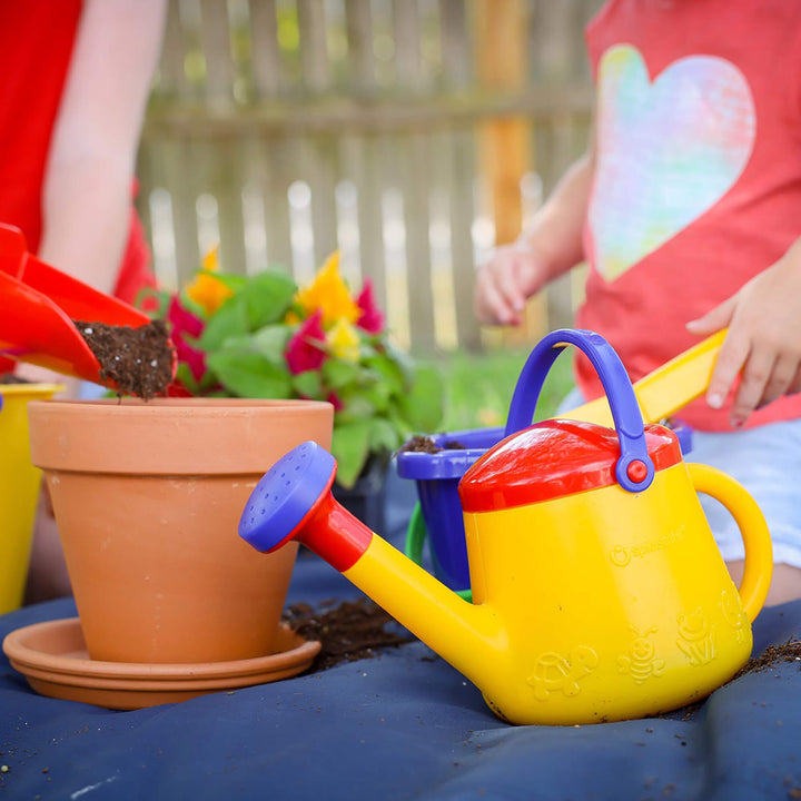 Spielstabil Watering Can sitting on table with terracotta pot and child standing behind
