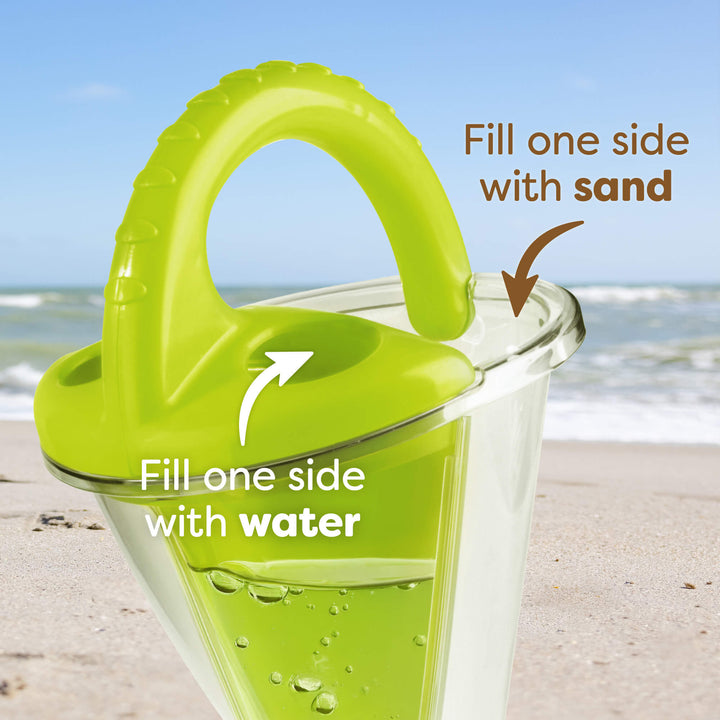 Close-up of a dual-compartment sand toy with a green handle on a beach. Text reads "Fill one side with sand and fill the other side with water."