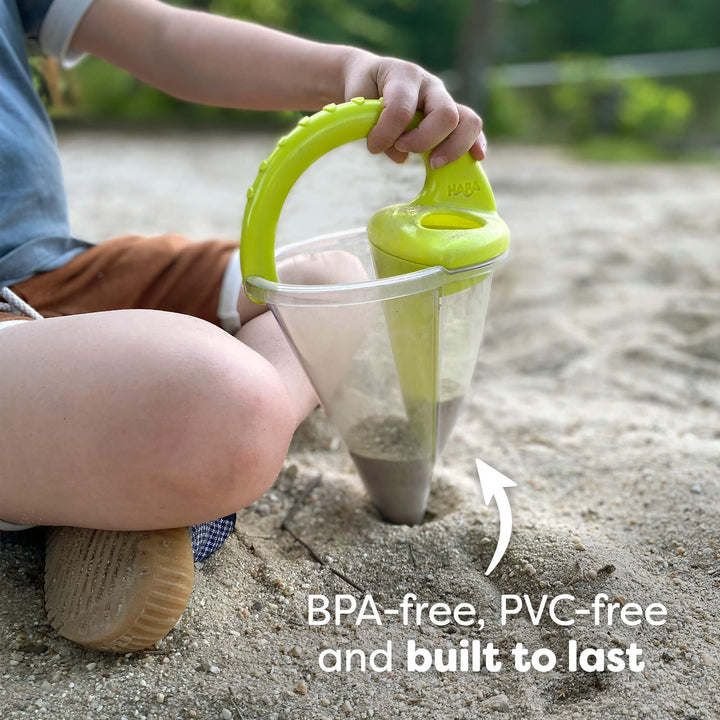 Child using a HABA Spilling Funnel with a green handle to dig in the sand. Text reads "BPA-free, PVC-free and built to last."