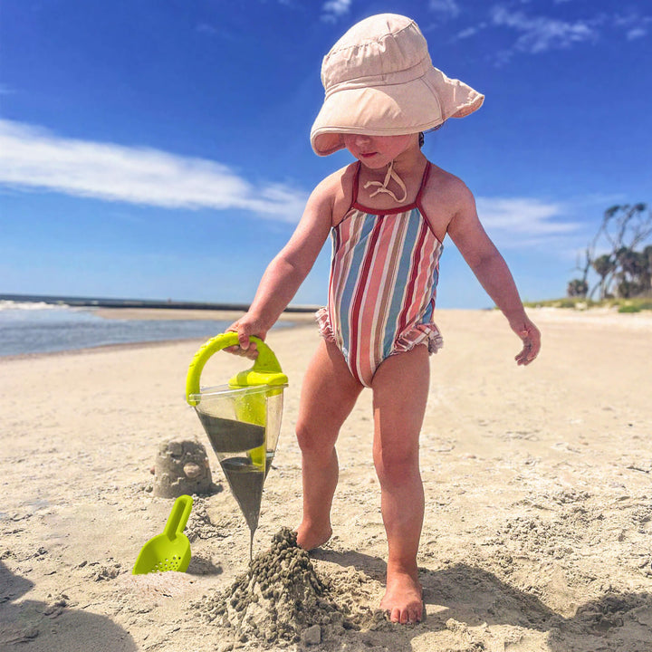 Child playing on a sunny beach with a sand funnel toy and shovel.