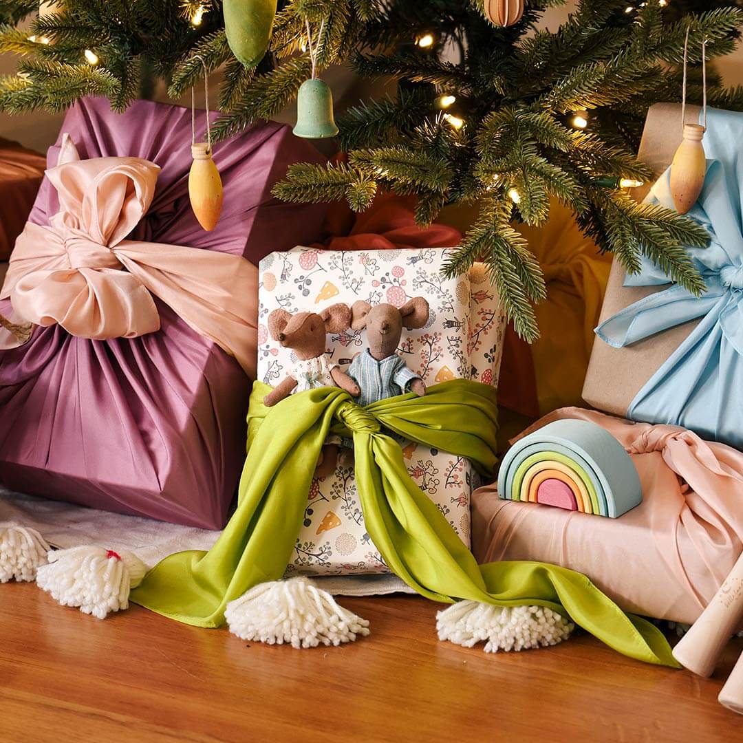 A package under a Christmas tree wrapped with silks with a wooden rainbow.