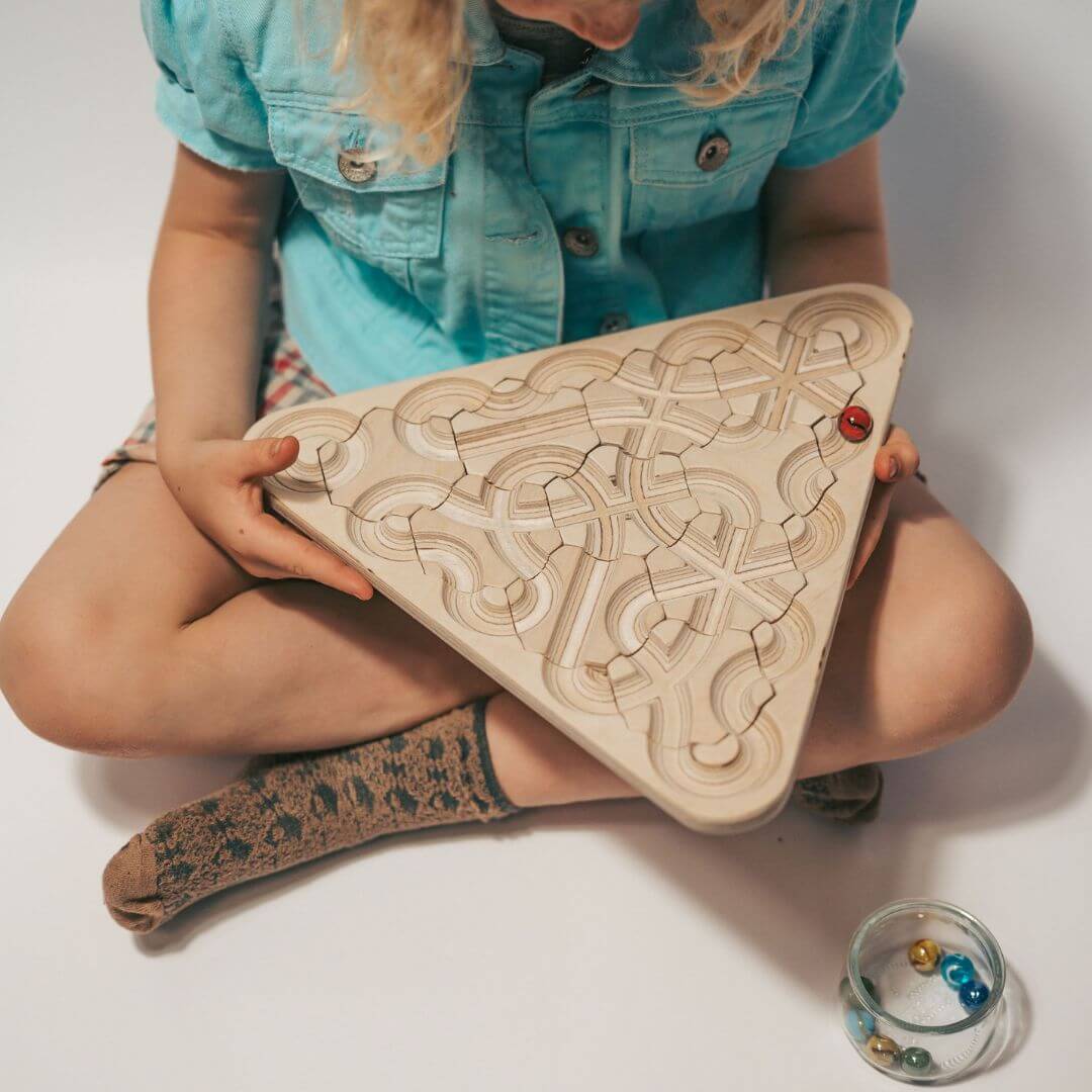 Child playing with wooden mindfulness marble maze with rearrangeable hexagon tiles arranged in a triangle board, featuring looping engraved pathways and colorful marbles - Bella Luna Toys