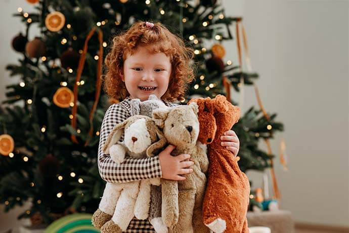 Child holding stuffed animals in front of a decorated Christmas tree