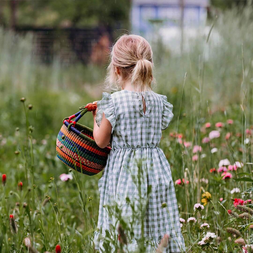A girl holding a bolga basket in a field of flowers.