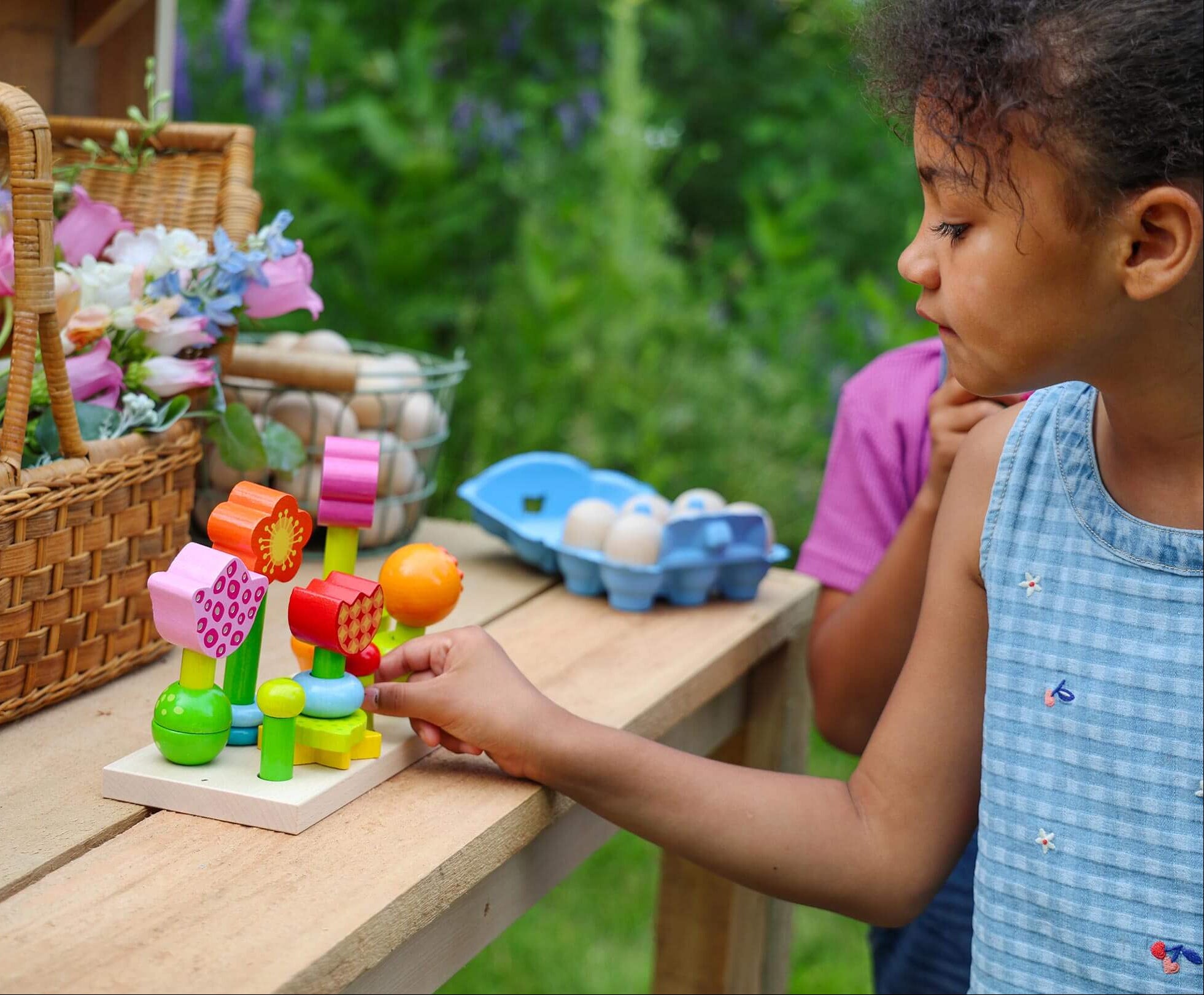 A girl is playing with a wooden flower set outside.