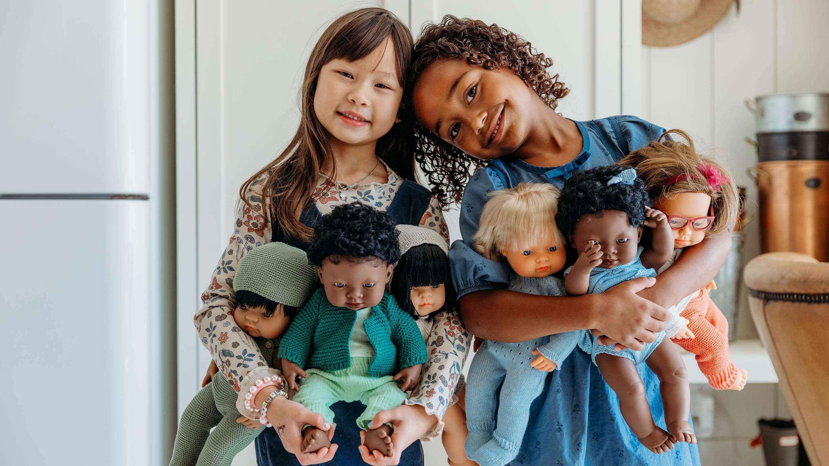 Two girls are holding a collection of dolls.