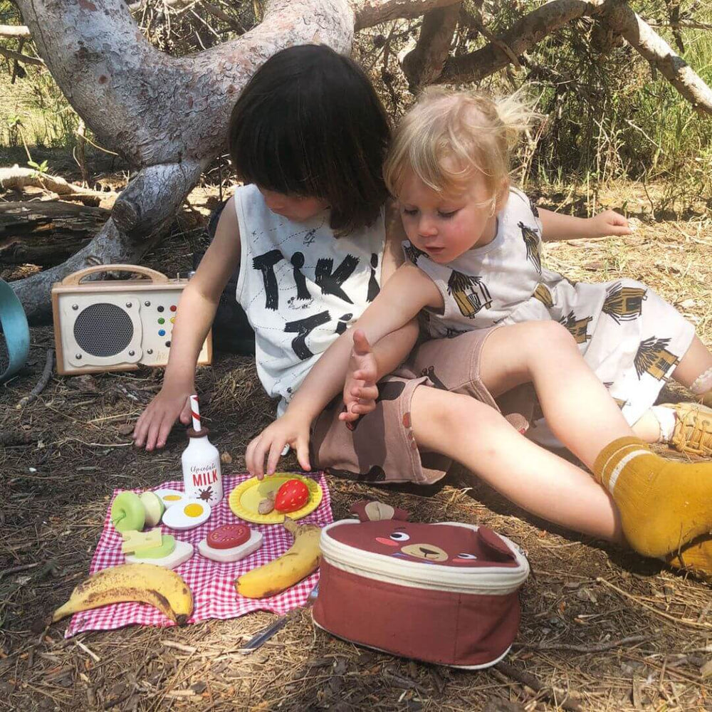 Tender Leaf Toys - Two children sitting on the ground with a picnic setup in a natural setting.