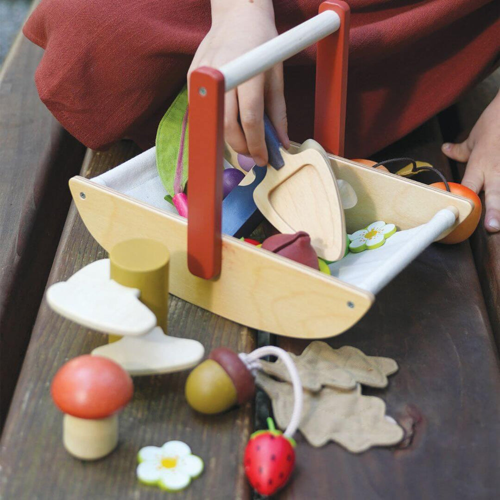 Child playing with a wooden toy fruit and vegetable set on a wooden surface.