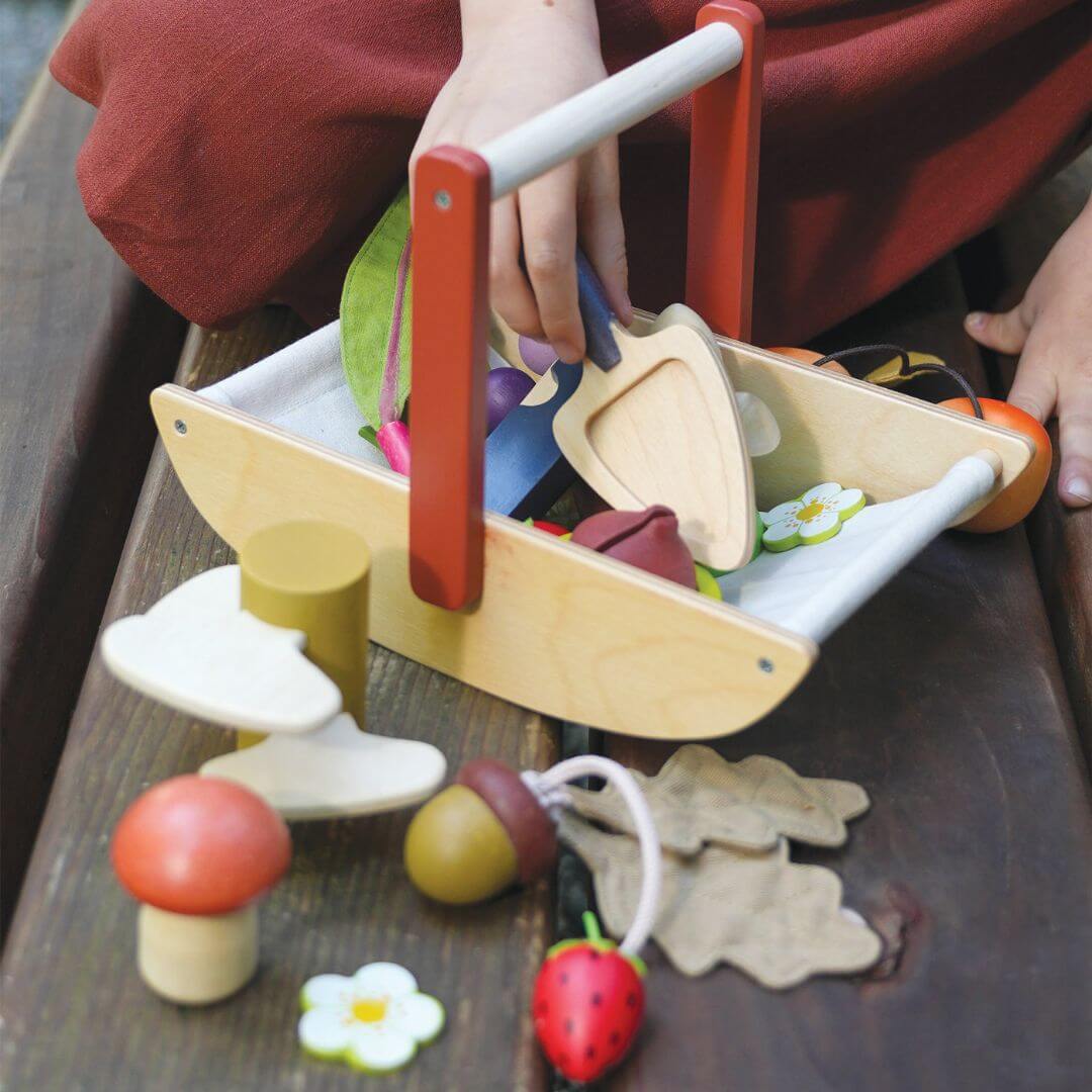 Child playing with a wooden toy fruit and vegetable set on a wooden surface.