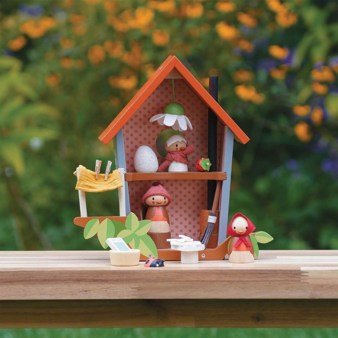 Miniature wooden Tender Leaf Toys bird dollhouse with a bird family on a wooden surface with a blurred natural background