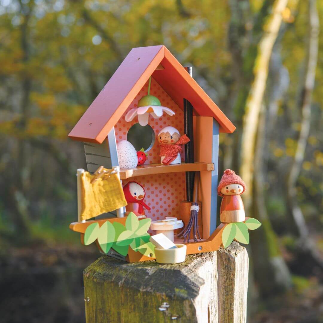 Colorful Tender Leaf Toys birdhouse with cartoon characters on a wooden post against a blurred natural background.