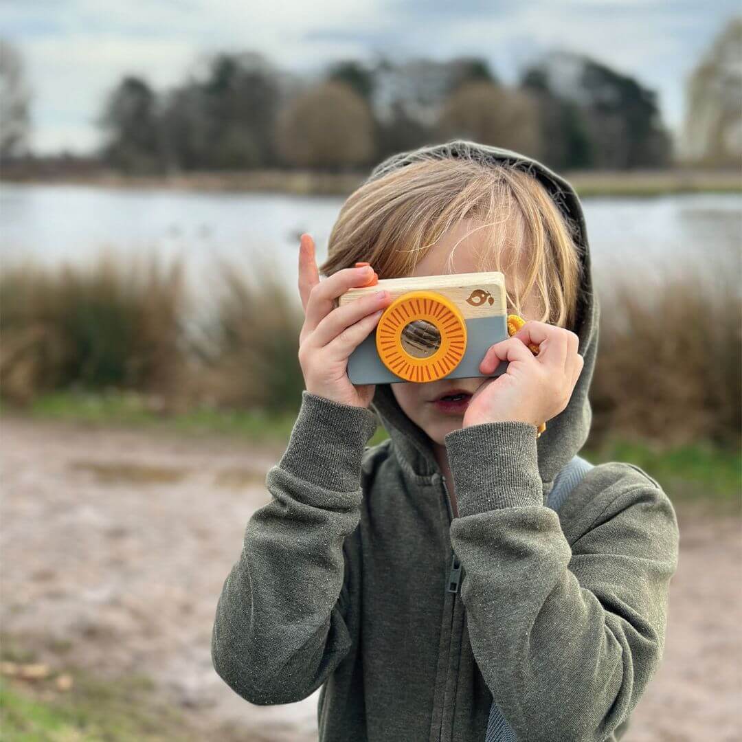 Child holding a toy camera outdoors near a lake