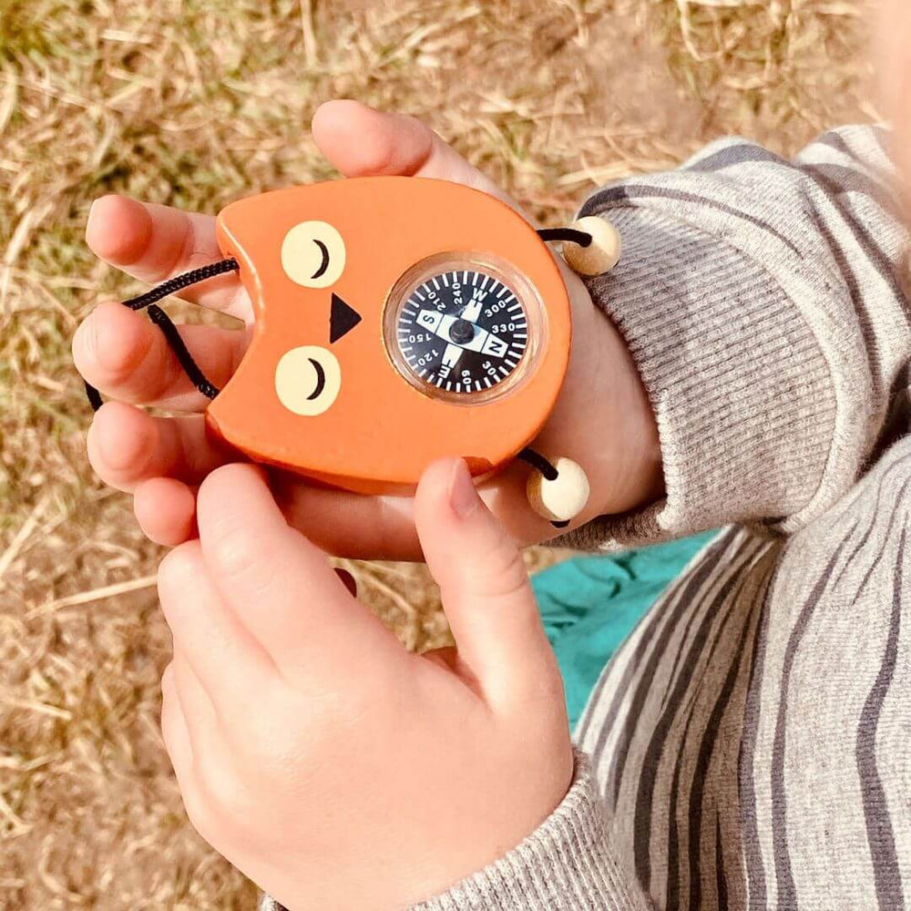 Hand holding an orange compass shaped like a cat with a blurred natural background