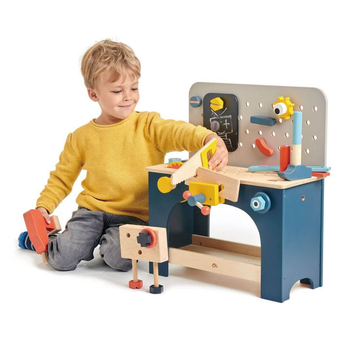 Child playing with a toy workbench and tools on a white background. Tender Leaf Toys