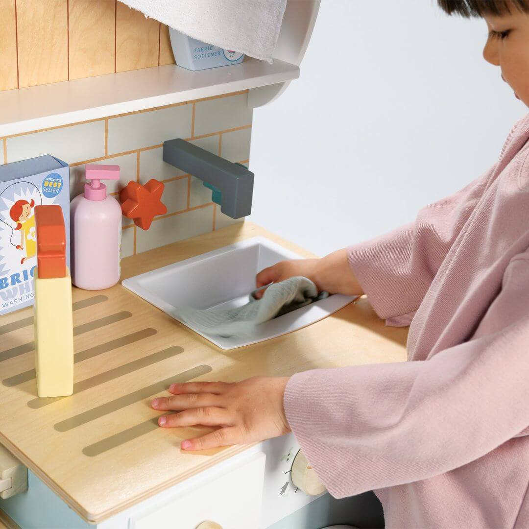 Child playing with a toy kitchen sink set in a child-sized kitchen.