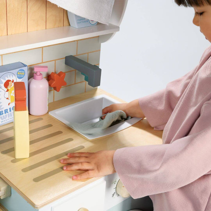 Child playing with a toy kitchen sink set in a child-sized kitchen.