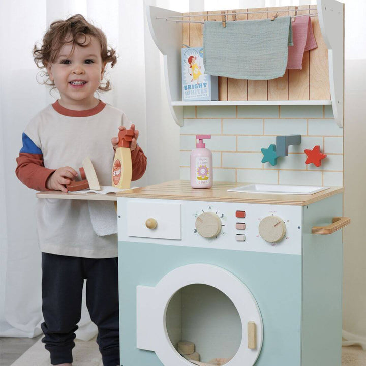 Child playing with a toy washing machine and dryer set in a kitchen-like setup.