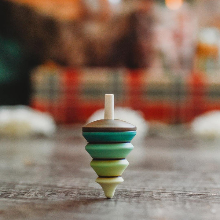 Colorful wooden top in the shape of a tree on a wooden surface with a blurred holiday background.