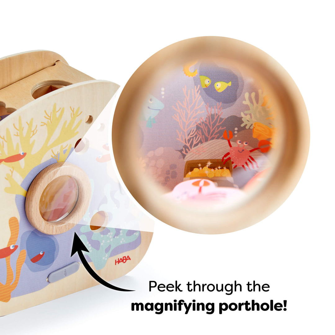 Wooden toy with underwater-themed illustrations and a magnified underwater scene showing sea creatures. Text reads "Peek through the magnifying porthole!"