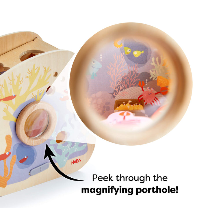 Wooden toy with underwater-themed illustrations and a magnified underwater scene showing sea creatures. Text reads "Peek through the magnifying porthole!"