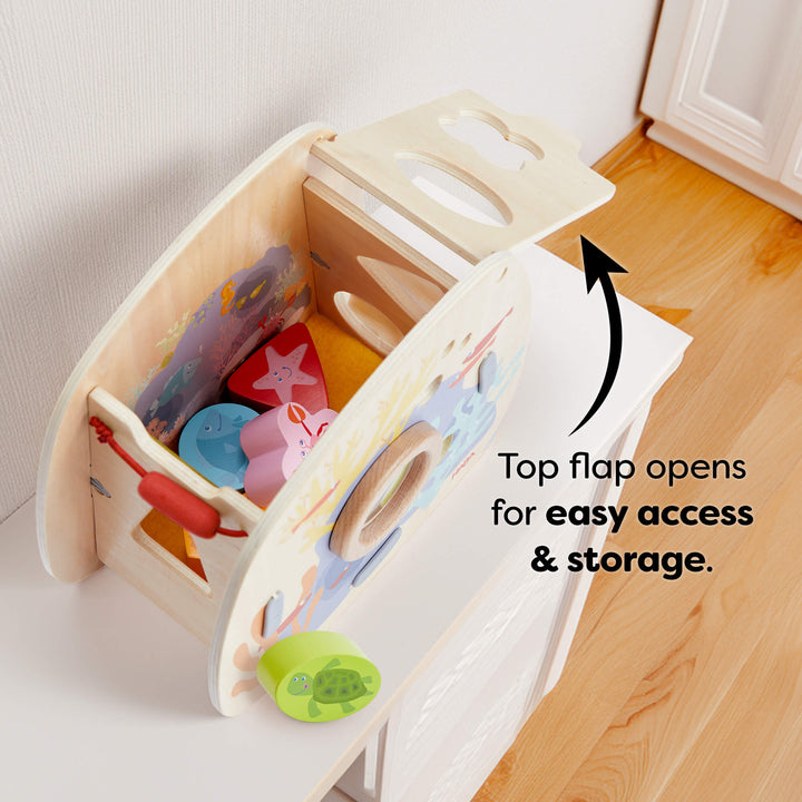 Open wooden toy box with colorful marine-themed blocks and an open top flap. Text reads "Top flap opens for easy access & storage."