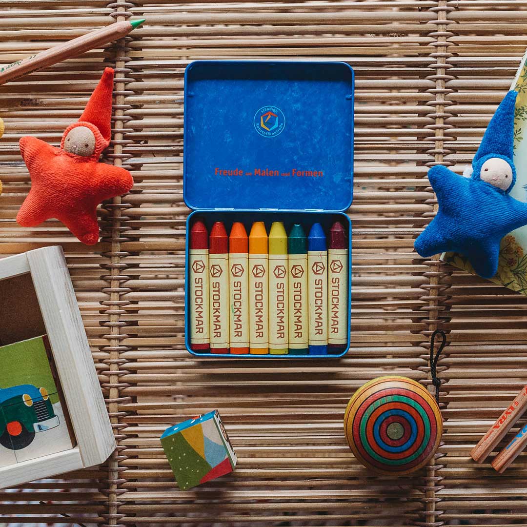 Colorful crayons in a tin box with toys on a woven surface