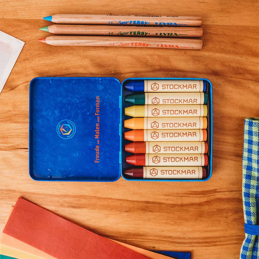 Set of Stockmar crayons in a blue tin on a wooden surface with pencils above.