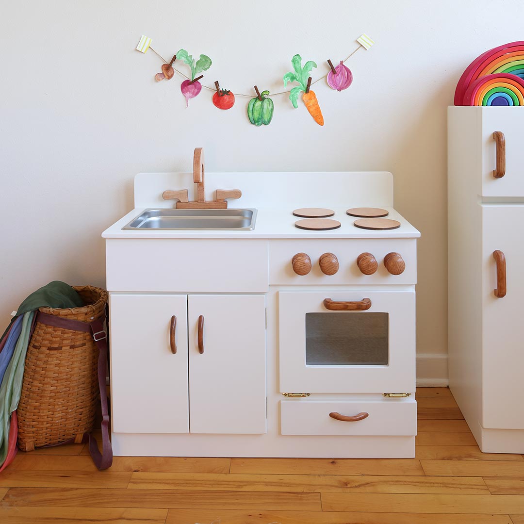 Children's play kitchen set with sink, stove, and cabinets on a wooden floor.