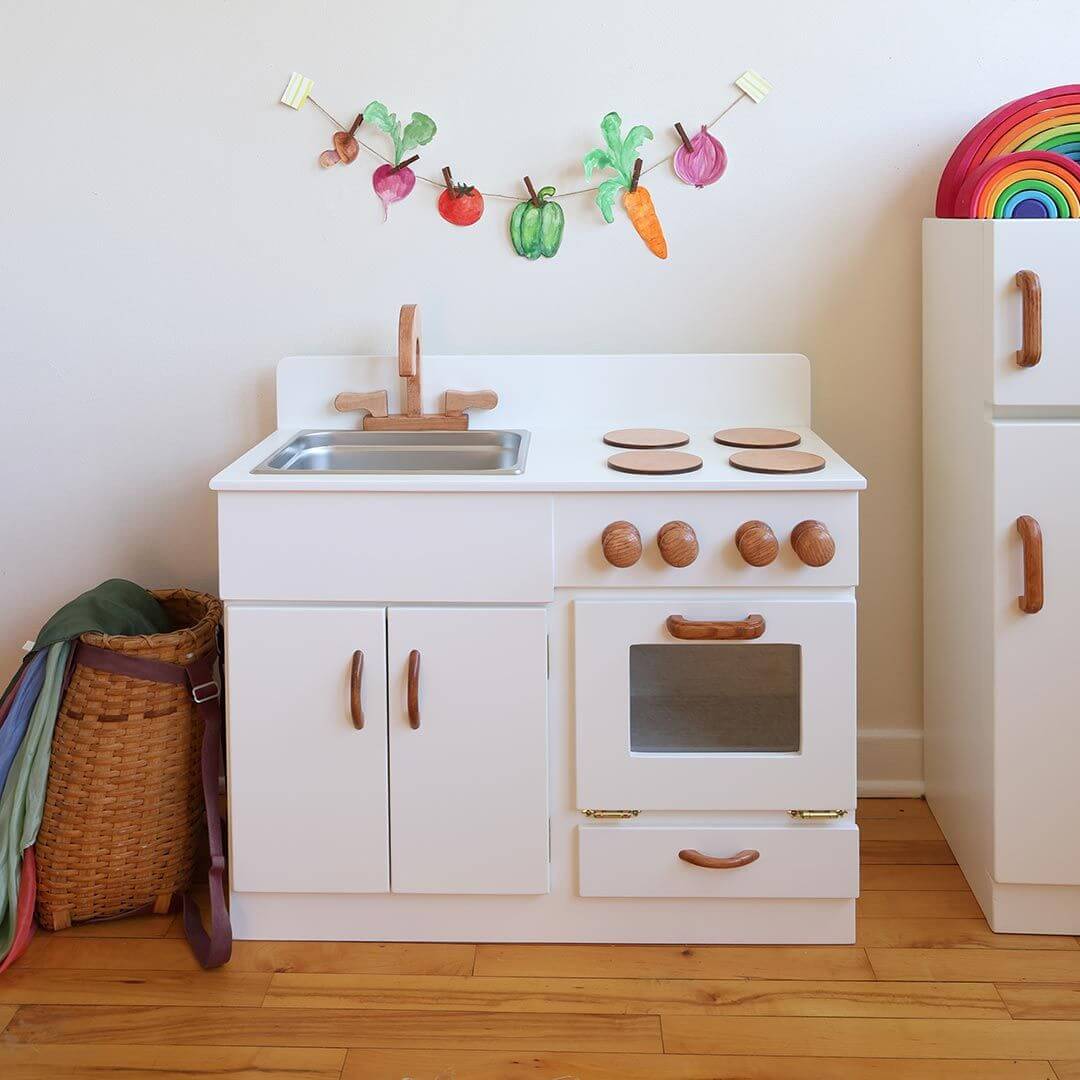 Children's play kitchen set with sink, stove, and cabinets on a wooden floor.