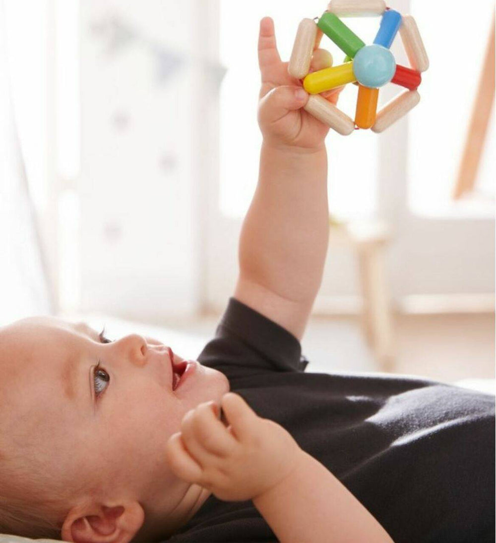 Baby holding Color Carousel Wooden Baby Rattle up in the air above them, looking at it