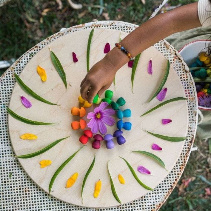 Child playing outside, arranging Grapat Mandala Wooden Rainbow Mushrooms on a round wooden tray with leaves and flower petals