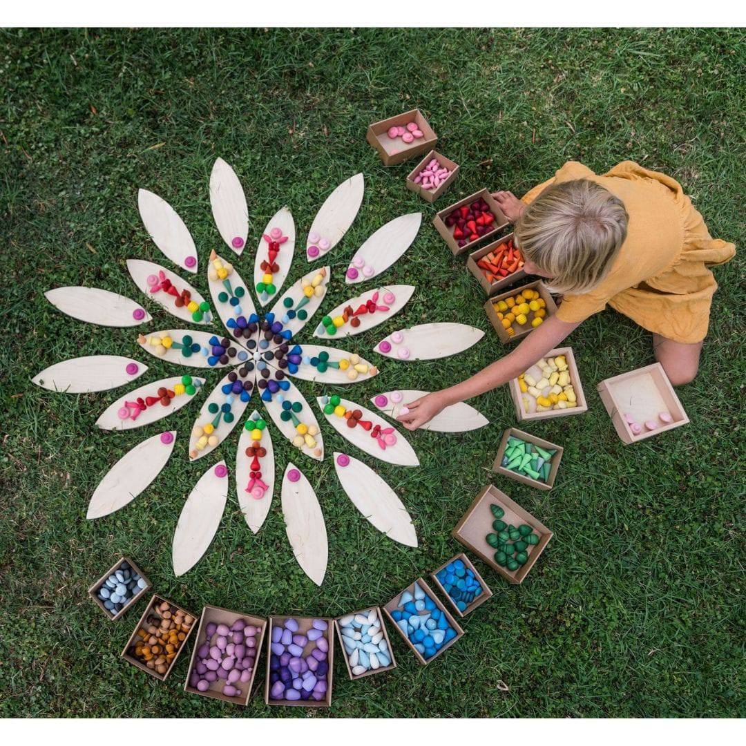 Child playing on grass with various colorful wooden Grapat pieces on Petal Platform, with petal-shaped pieces arranged into shape of flower