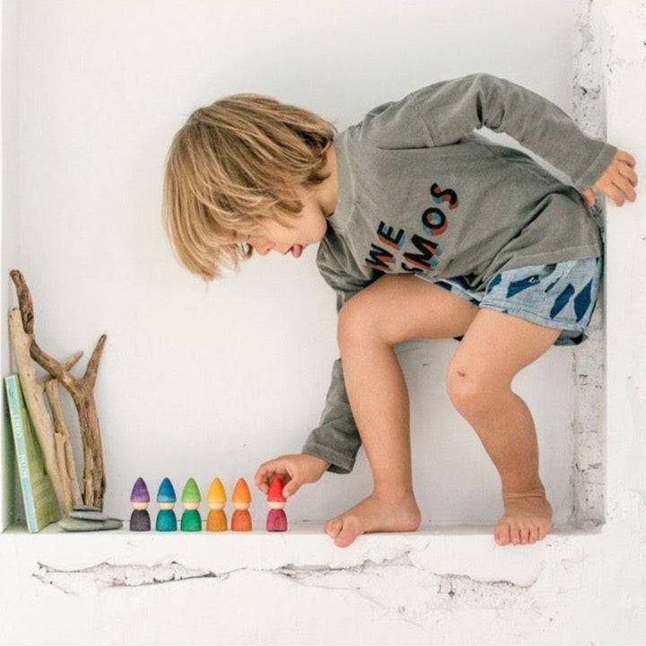 Child playing, lining up Grapat Wooden Rainbow Tomtens on a shelf ledge