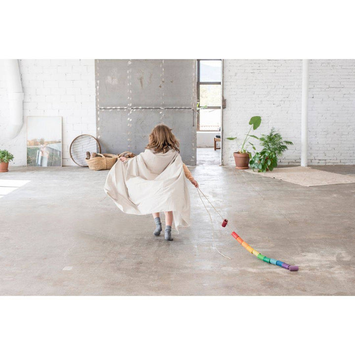 Child playing with rainbow tubes on a string, pulling them across a room in a cape