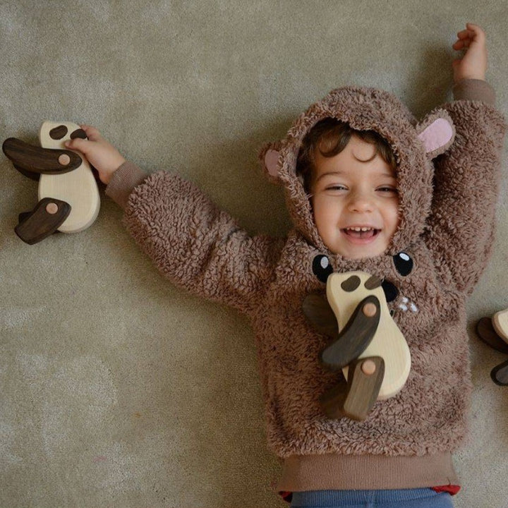 Bajo- Smiling child laying on the floor playing with three Wooden Pandas- Bella Luna Toys